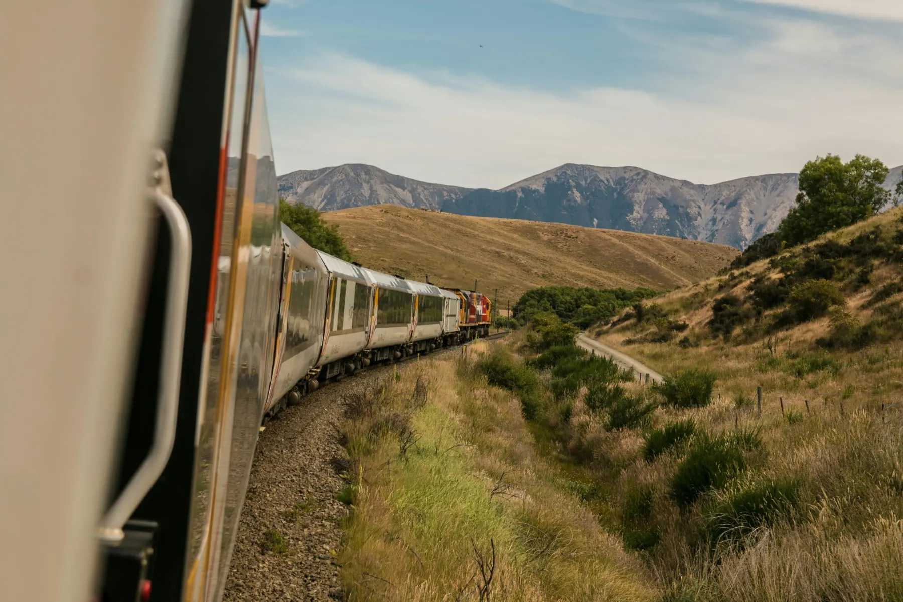 Passenger train curving through hills towards the mountains